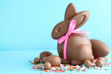 Çikolatalı Paskalya tavşanı, yumurtalar, şekerler ve açık mavi arka planda serpiştirmeler. Metin için boşluk