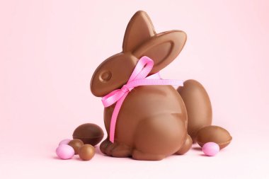 Çikolatalı Paskalya tavşanı ve pembe arka planda şekerli yumurtalar, yakın plan.