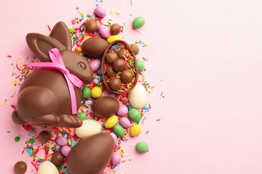 Çikolatalı Paskalya tavşanı, yumurtalar, şekerler ve pembe arka plana serpiştirilmiş şekerler, düz yatak. Metin için boşluk