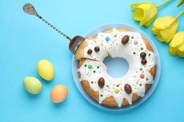 Lezzetli Paskalya pastası, boyanmış yumurtalar ve açık mavi arka planda sarı laleler, düz uzanmış.