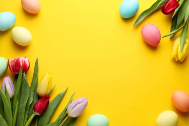 Boyalı Paskalya yumurtaları ve sarı arka planda güzel laleler. Metin için boşluk
