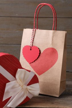 Kese kağıdı ve kalp şeklinde hediye paketi ahşap masada, yakın plan.