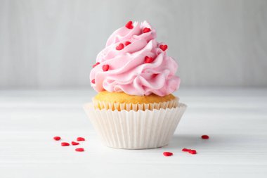 Sevgililer Günün kutlu olsun. Gri duvarın yakınındaki beyaz ahşap masada kalp şeklinde serpiştirilmiş lezzetli kek.