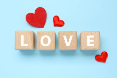 Aşk sözcüğüyle ahşap küpler ve açık mavi arka planda kırmızı kalpler, düz yatış. Tebrik kartı