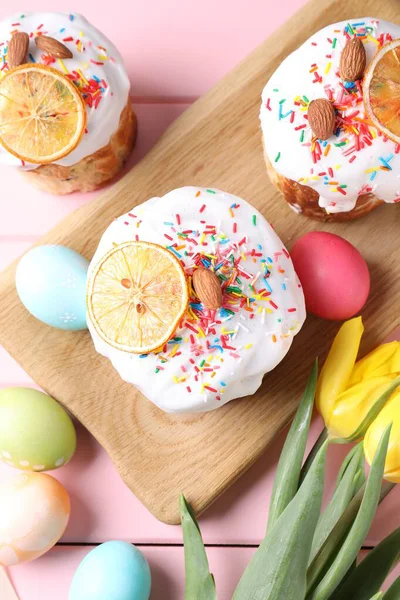 Lezzetli Paskalya pastaları, laleler ve pembe ahşap masaya boyanmış yumurtalar.