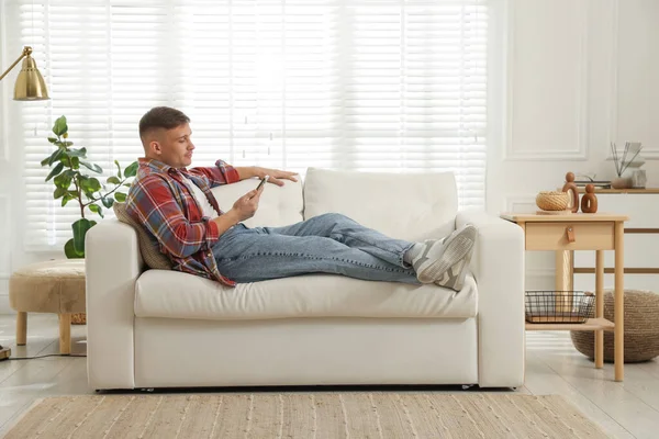 Akıllı telefonlu genç adam evdeki kanepede dinleniyor.