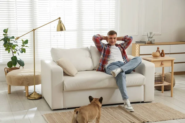 Genç adam kanepede dinleniyor ve evde sevimli bir köpek var.