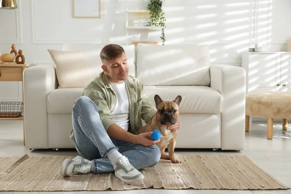 Evdeki kanepenin yanında sevimli köpeği ve oyuncağıyla genç bir adam.