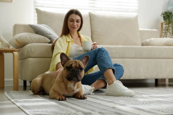 Şirin köpeği ve bir bardak içkisi olan bir kadın evdeki kanepenin yanında dinleniyor, seçici bir şekilde odaklanıyor.