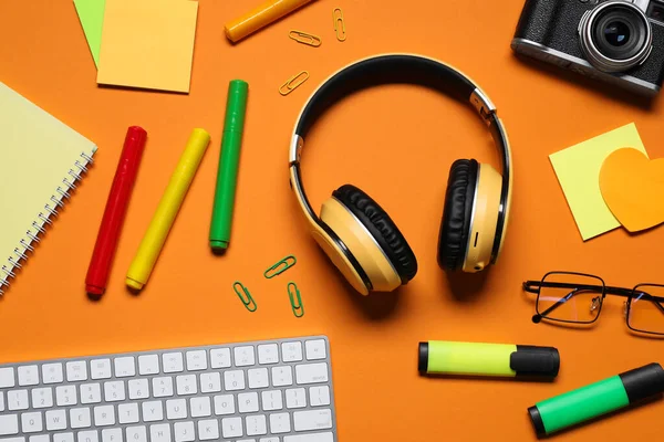 Kulaklıklar, bilgisayar klavyesi, klasik kamera, turuncu arka planda gözlük ve kırtasiye malzemesi, düz konum