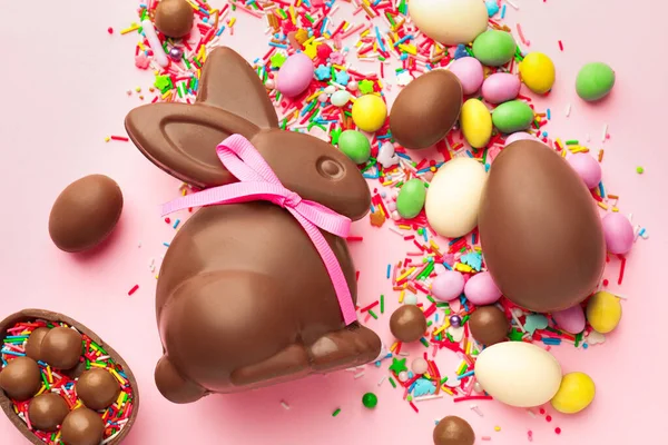 Çikolatalı Paskalya tavşanı, yumurtalar, şekerler ve pembe arka planda serpiştirilmiş şekerler.
