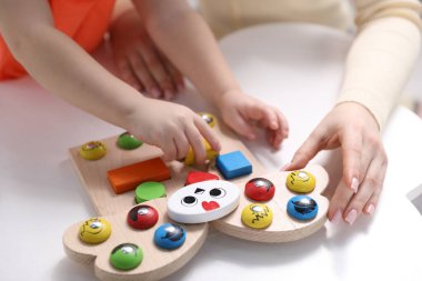 Anne ve oğlu içeride beyaz masada oyuncaklarla oynuyorlar, yakın plan.