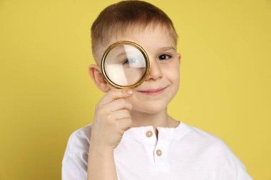 Sarı arka planda büyüteç olan küçük çocuk.