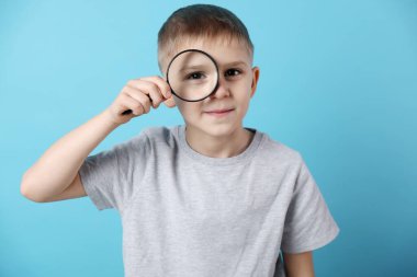 Açık mavi arka planda büyüteç takan küçük çocuk.