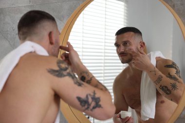 Evdeki aynanın yanında yüzüne krem süren yakışıklı bir adam.