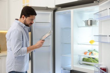 Mutfakta açık buzdolabının yanında çiğ eti olan bir adam.