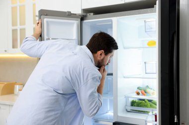Mutfaktaki boş buzdolabına bakan bir adam.