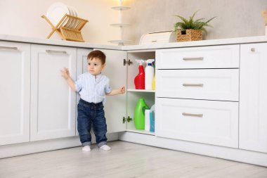 Evde çocuk güvenliği. Küçük çocuk mutfakta temizlik ürünleriyle dolap açıyor.