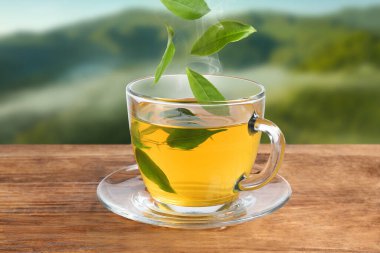 Dağlardaki masada taze demlenmiş çay. Yeşil yapraklar fincanın üzerinde uçuyor