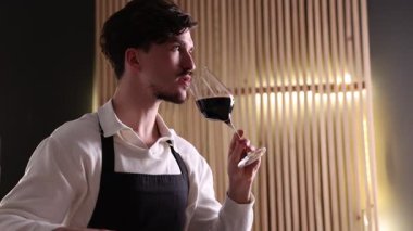 Profesyonel şarap garsonu kırmızı şarap tadıyor ve kapalı mekanlarda tadımlık kartı dolduruyor.