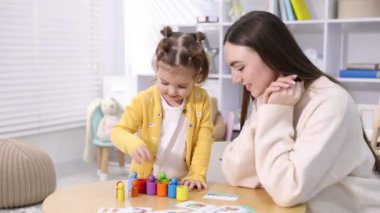 Anne ve kızı içeride tahta masada oyuncaklarla oynuyorlar.