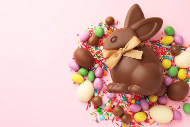 Çikolatalı Paskalya tavşanı, yumurtalar, şekerler ve pembe arka plana serpiştirilmiş şekerler, düz yatak. Metin için boşluk