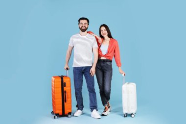 Açık mavi arka planda bavulları olan mutlu çift.