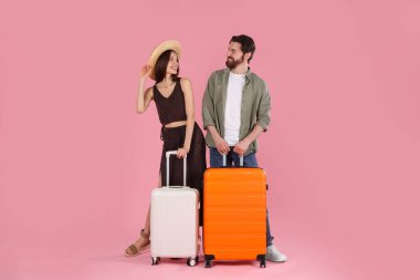 Pembe arka planda bavulları olan mutlu çift.