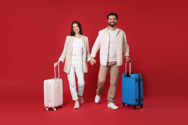 Kırmızı arka planda bavulları olan mutlu çift.