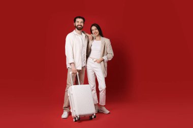 Kırmızı arka planda bavulu olan mutlu çift.