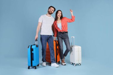 Açık mavi arka planda bavulları olan mutlu çift.