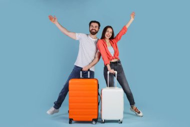 Açık mavi arka planda bavulları olan mutlu çift.