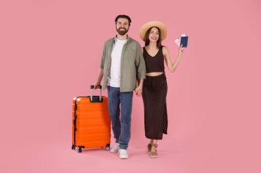 Bavulu, pasaportu ve pembe arka planda biletleri olan mutlu çift.