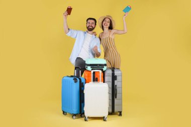 Bavulları, pasaportları ve sarı arka planda biletleri olan mutlu çift.