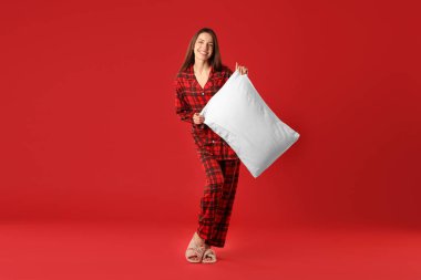 Kırmızı arka planda yastıklı şık pijamalı mutlu kadın.