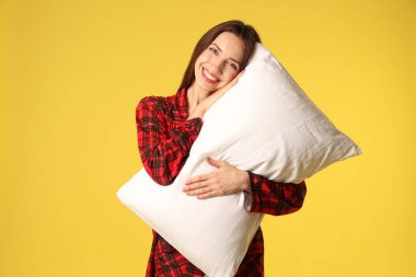 Sarı arka planda yastıklı şık pijamalı mutlu kadın.