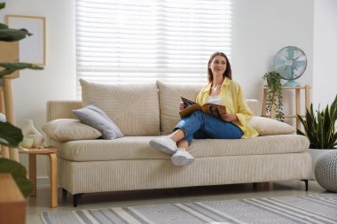 Dergisi olan kadın evinde kanepenin yanında dinleniyor, mesaj için yer var.