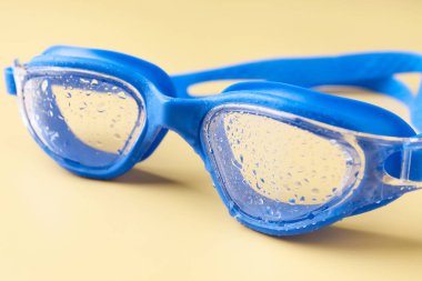 Sarı arka planda su damlaları olan yüzme gözlükleri, yakın plan