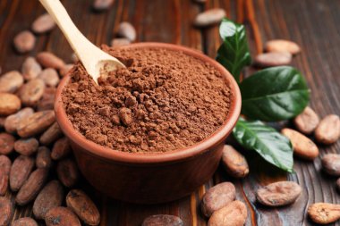 Doğal kakao çekirdekleri, toz ve yeşil yapraklar ahşap masada, yakın plan.