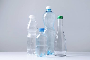 Beyaz masada gri arka planda farklı boyutlarda su şişeleri