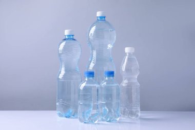 Beyaz masada gri arka planda farklı boyutlarda su şişeleri