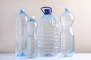 Beyaz masada bej arka planda farklı boyutlarda su şişeleri