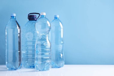 Beyaz masada açık mavi arka planda farklı boyutlarda su şişeleri var. Metin için boşluk