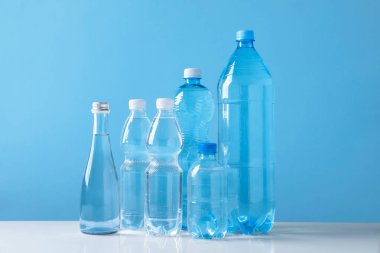 Açık mavi arka planda beyaz masada farklı boyutlarda su şişeleri