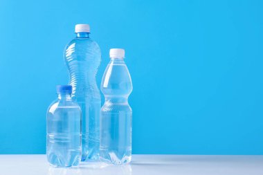 Beyaz masada farklı boyutlarda su şişeleri açık mavi arkaplan, metin için boşluk