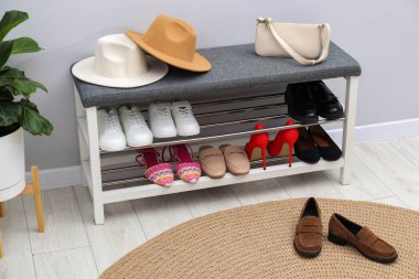 Farklı ayakkabı, aksesuarlar ve açık gri duvarın yanındaki ev bitkilerinden oluşan ayakkabı deposu.