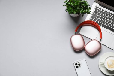 Kulaklıklar, dizüstü bilgisayarlar, kahve, akıllı telefon ve açık gri arka planda çiçekli dekor. Metin için boşluk
