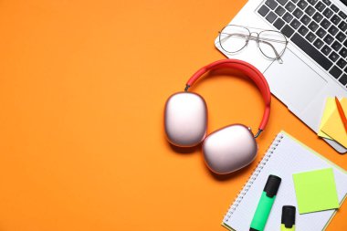 Kulaklık, laptop, gözlük ve kırtasiye malzemesi turuncu arka planda, düz konum. Metin için boşluk