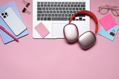 Kulaklık, akıllı telefon, dizüstü bilgisayar, pembe arka planda gözlük ve kırtasiye malzemesi. Metin için boşluk