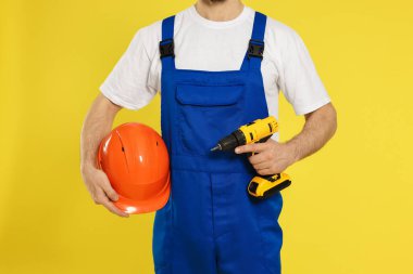 Sarı arka planda baret ve vida tabancası olan profesyonel müteahhit, yakın plan.